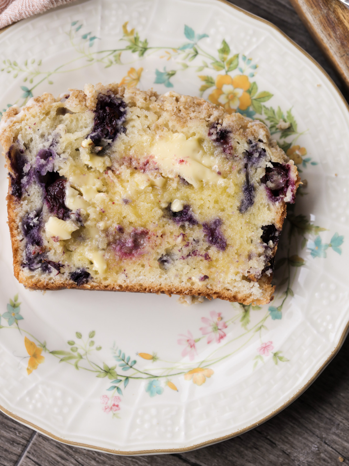 Once slice of buttered sourdough discard blueberry crumble bread sits on a floral plate.