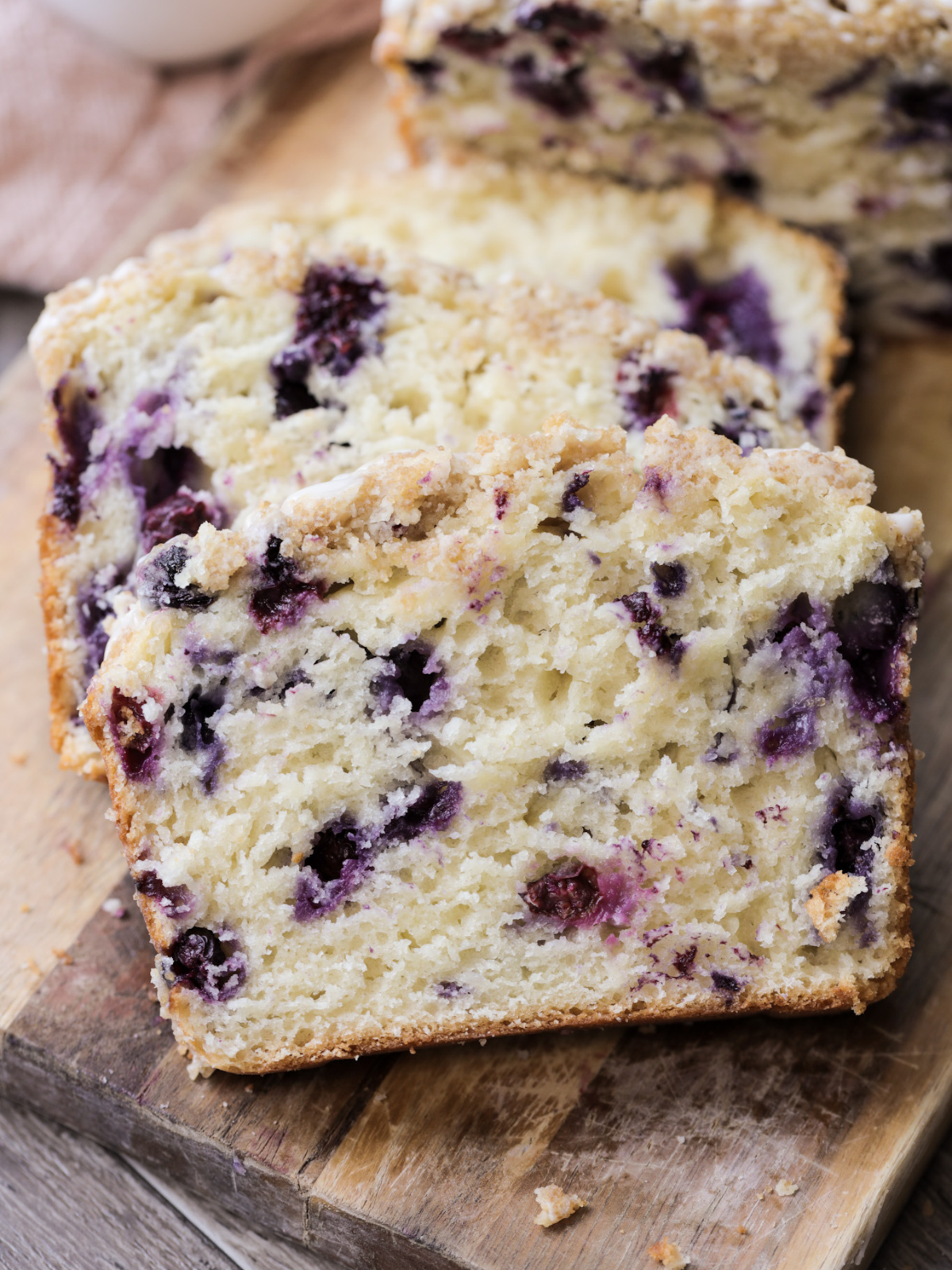 A closeup of two sourdough discard blueberry crumble loaf slices sit on a wooden cutting board.