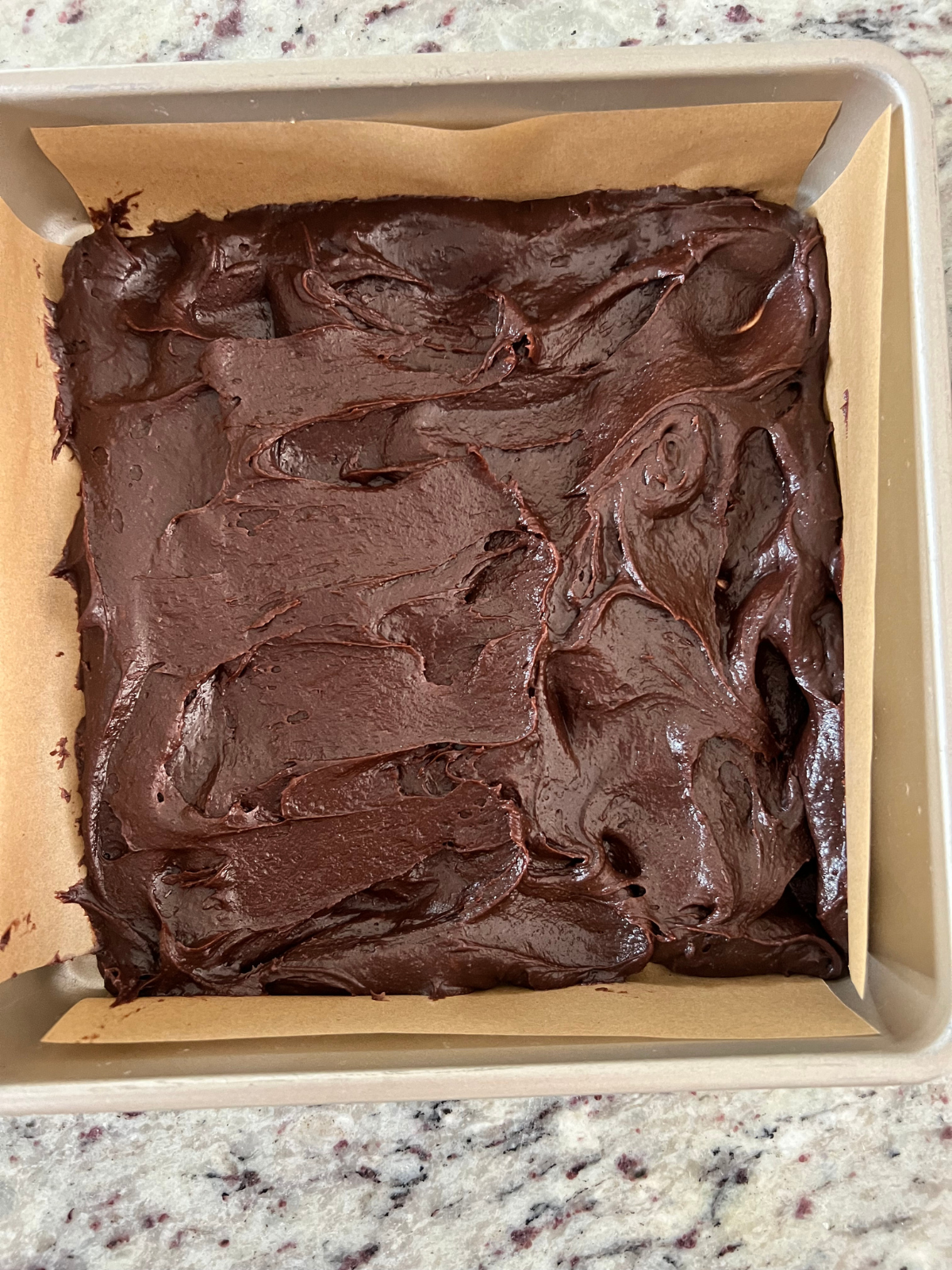 Half the sourdough brownie batter is shown in the parchment paper lined baking pan.