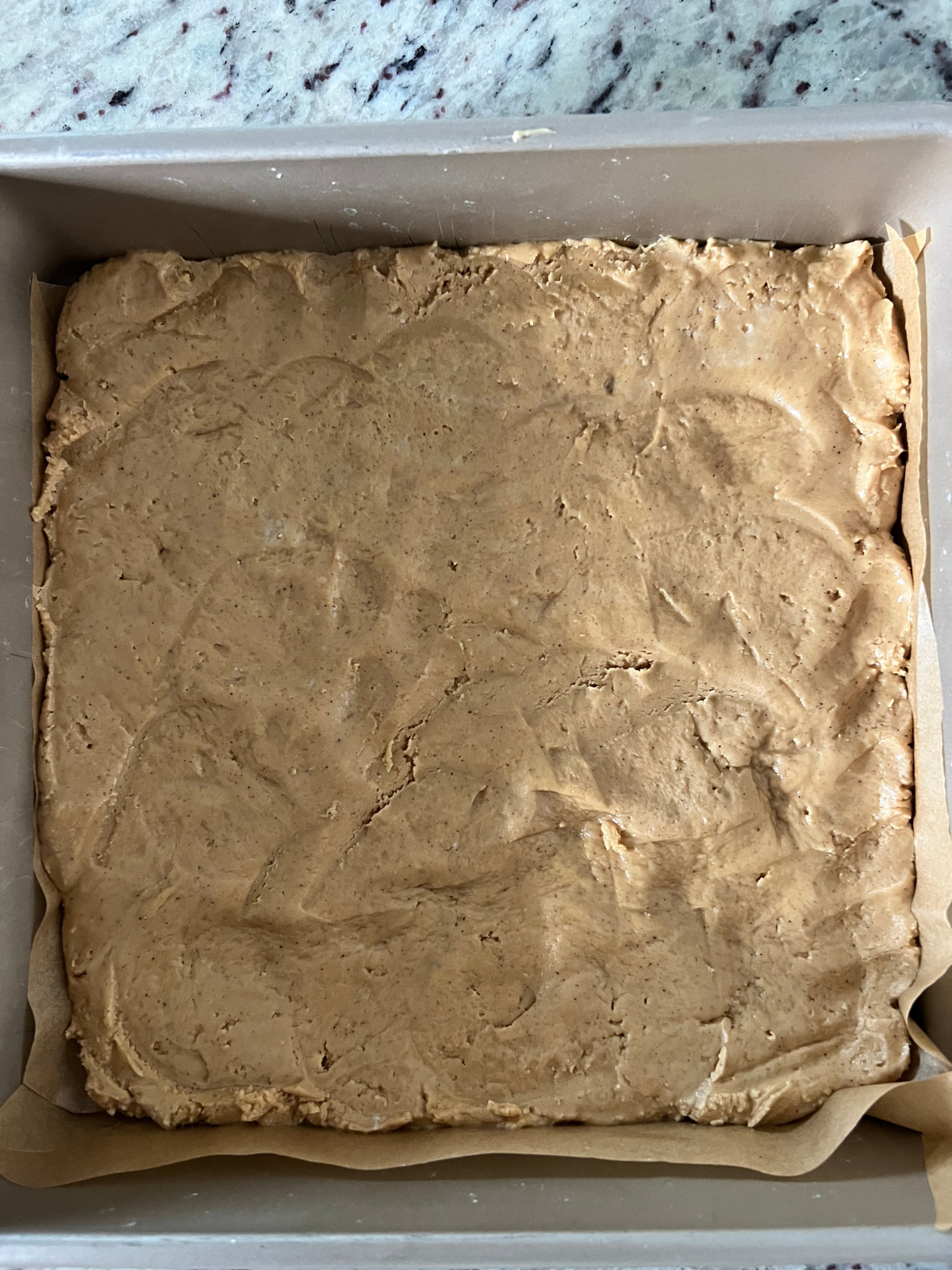 The peanut butter filling is shown pressed into a parchment paper lined 9x9 baking pan.