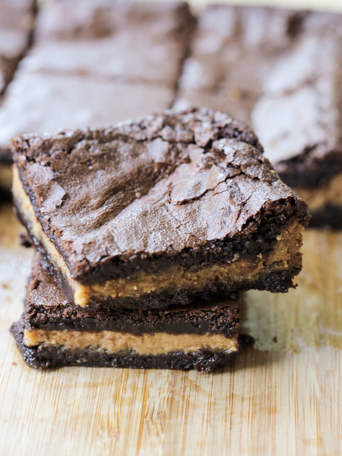 Two sourdough brownies with peanut butter filling are shown stacked with several more sourdough discard peanut butter brownies in the background.
