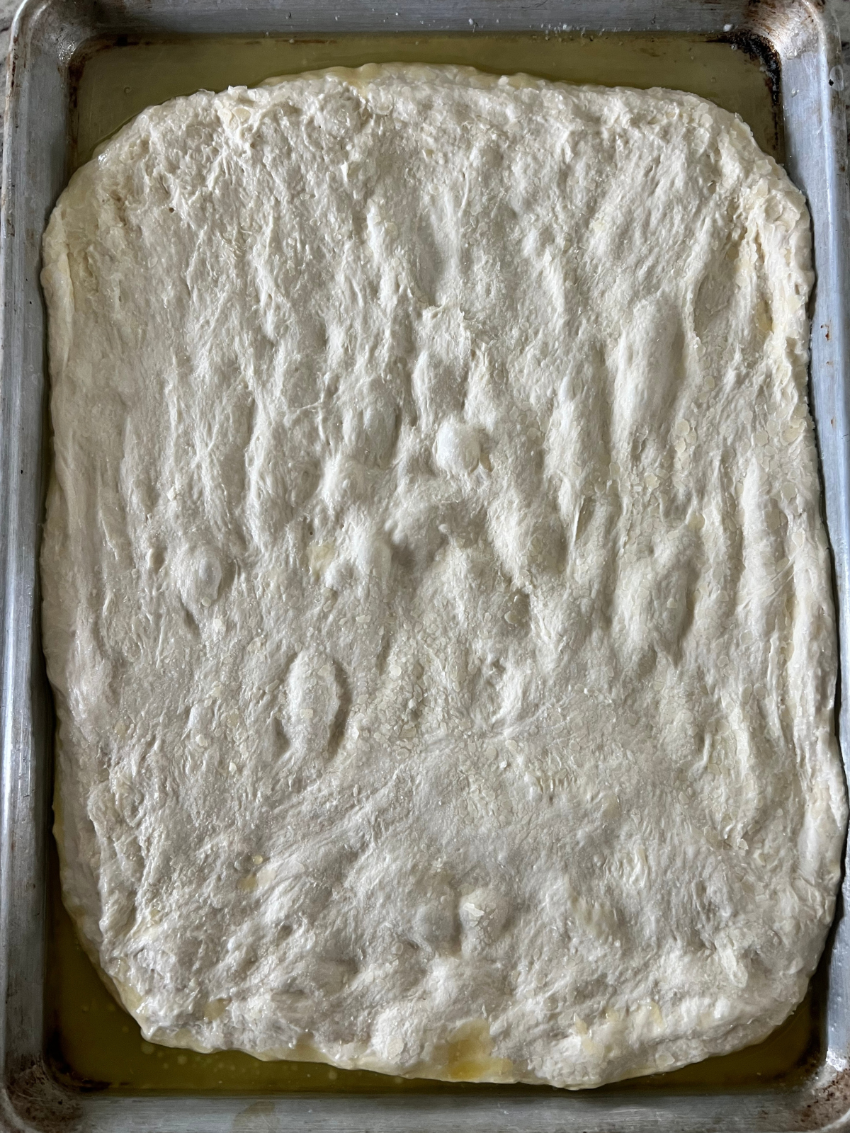 The sourdough focaccia is shown stretched out over the baking sheet.