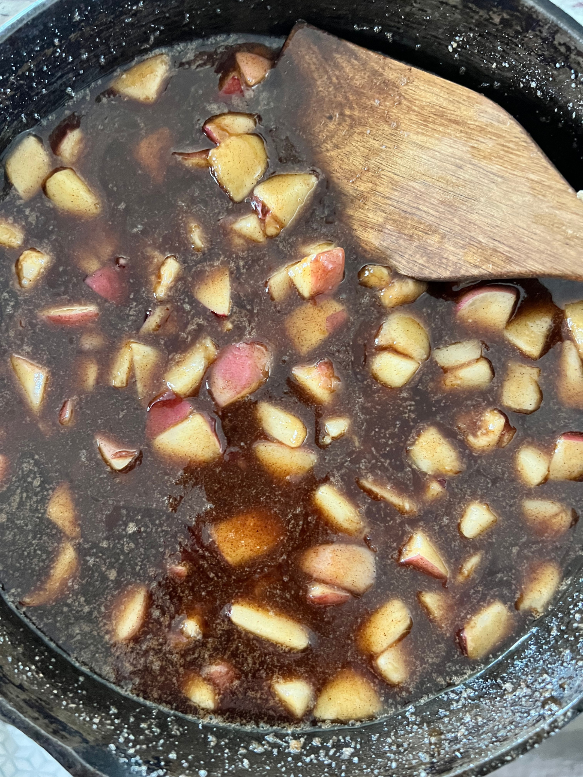 The brown sugar butter peach filling is shown cooking over the stove in a cast iron skillet. 