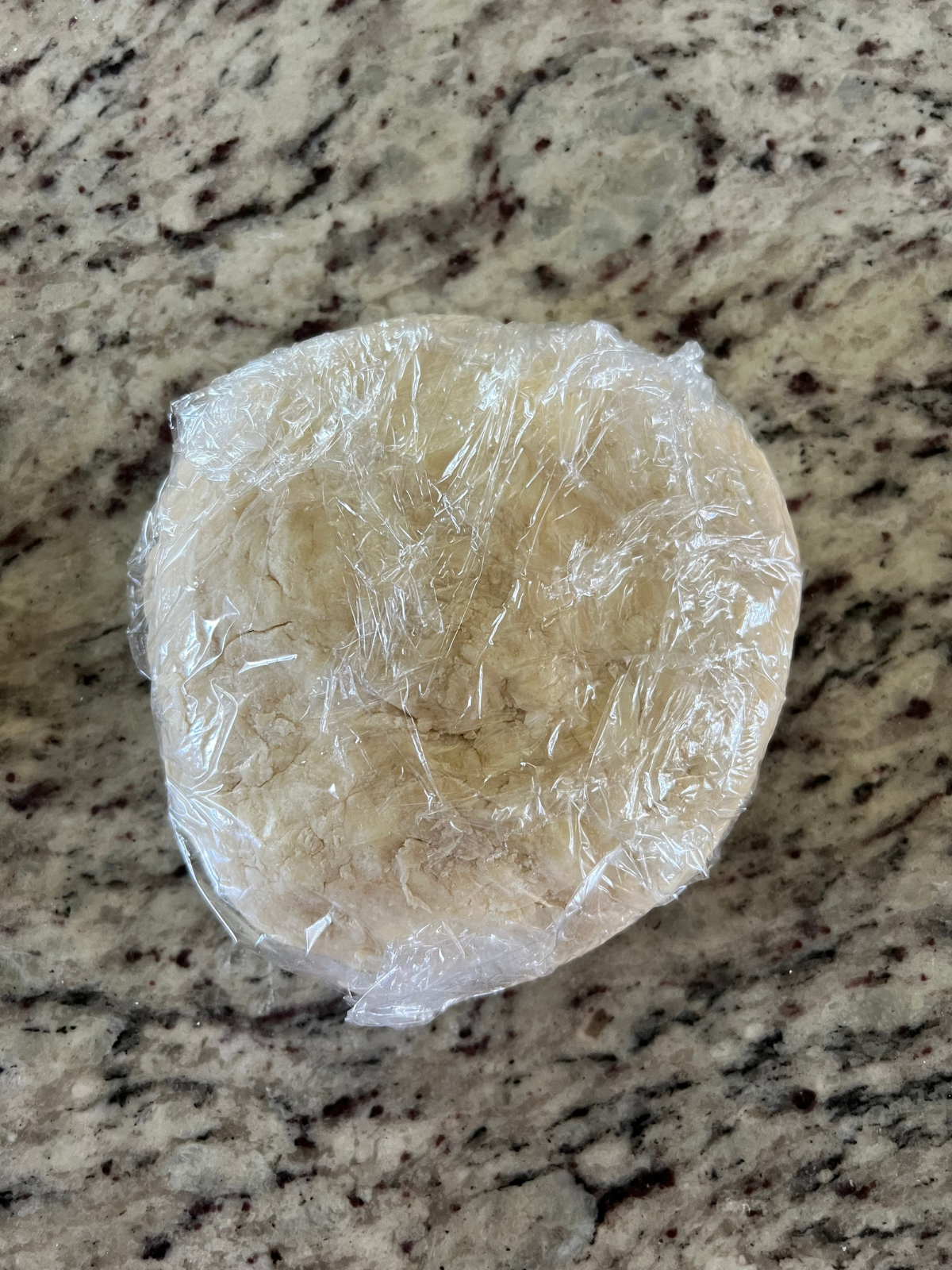 Sourdough discard hot pocket dough is shaped into a disc and shown with plastic wrap before chilling in the fridge.