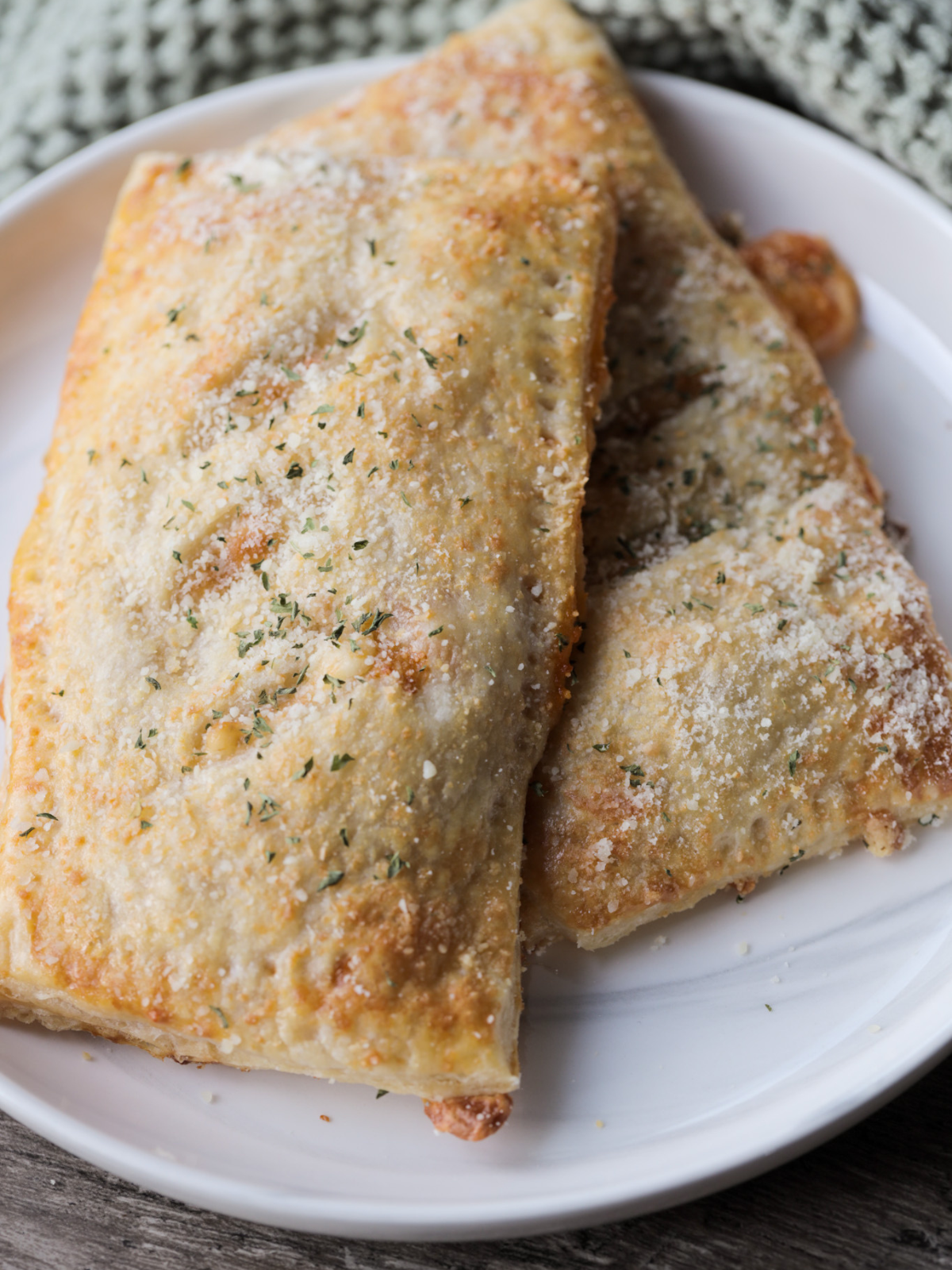 Sourdough pepperoni pizza hot pockets with parmesan cheese, dried parsley and gooey mozzarella cheese sit on a plate.