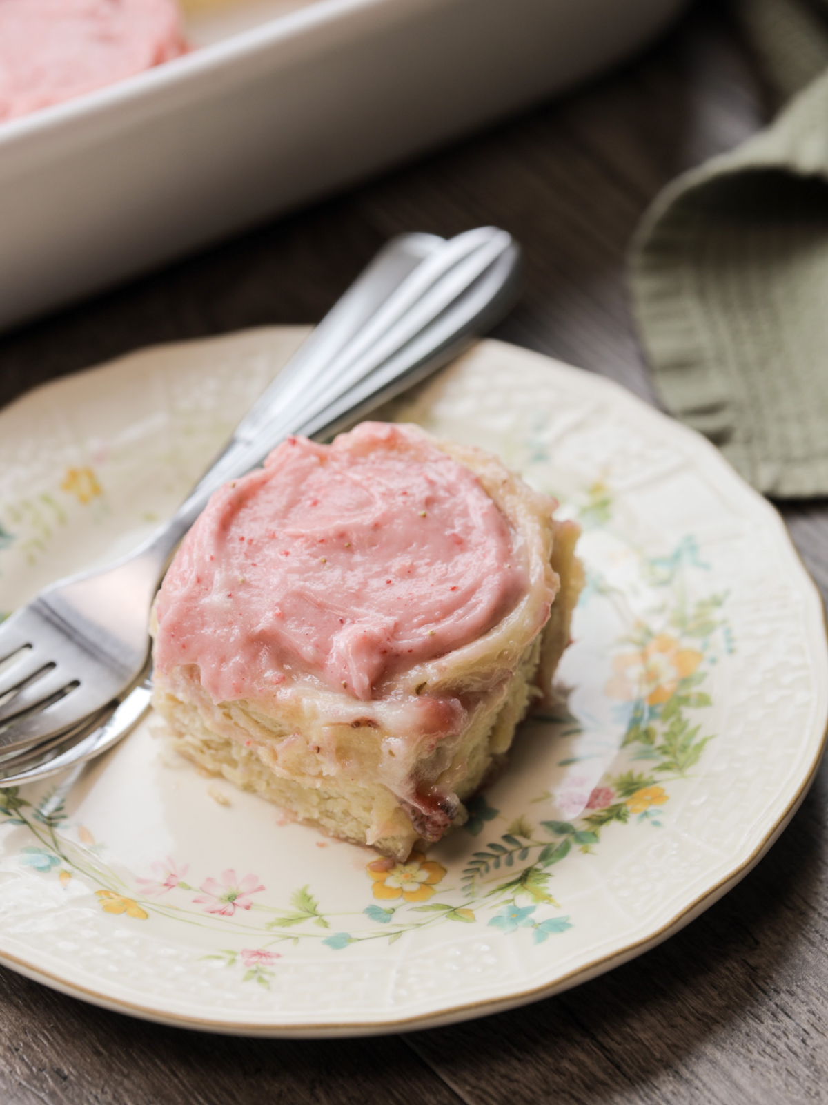 A sourdough strawberry cheesecake sweet roll sits on a floral plate. 