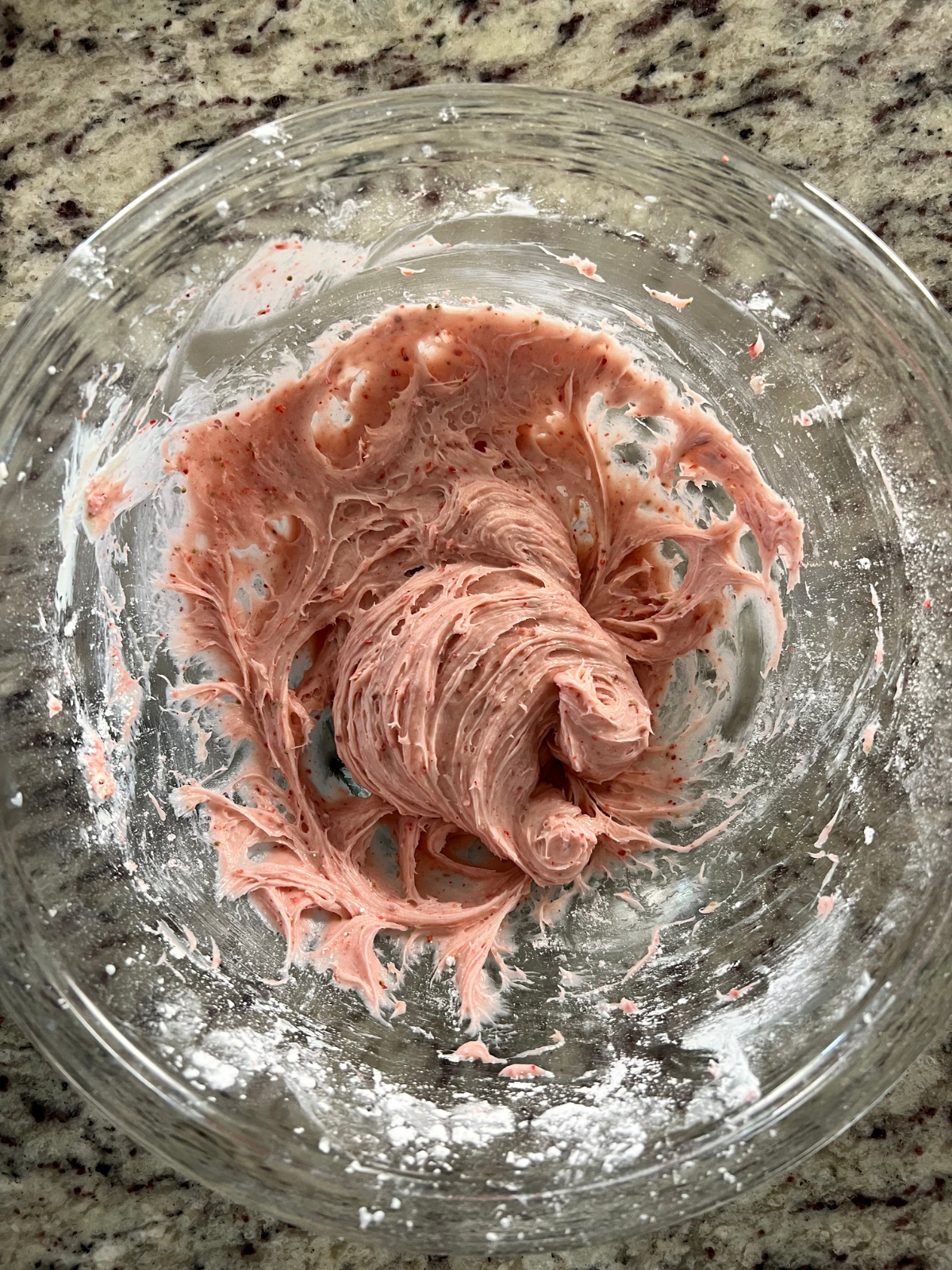 The strawberry cream cheese frosting is shown mixed together in a glass mixing bowl.