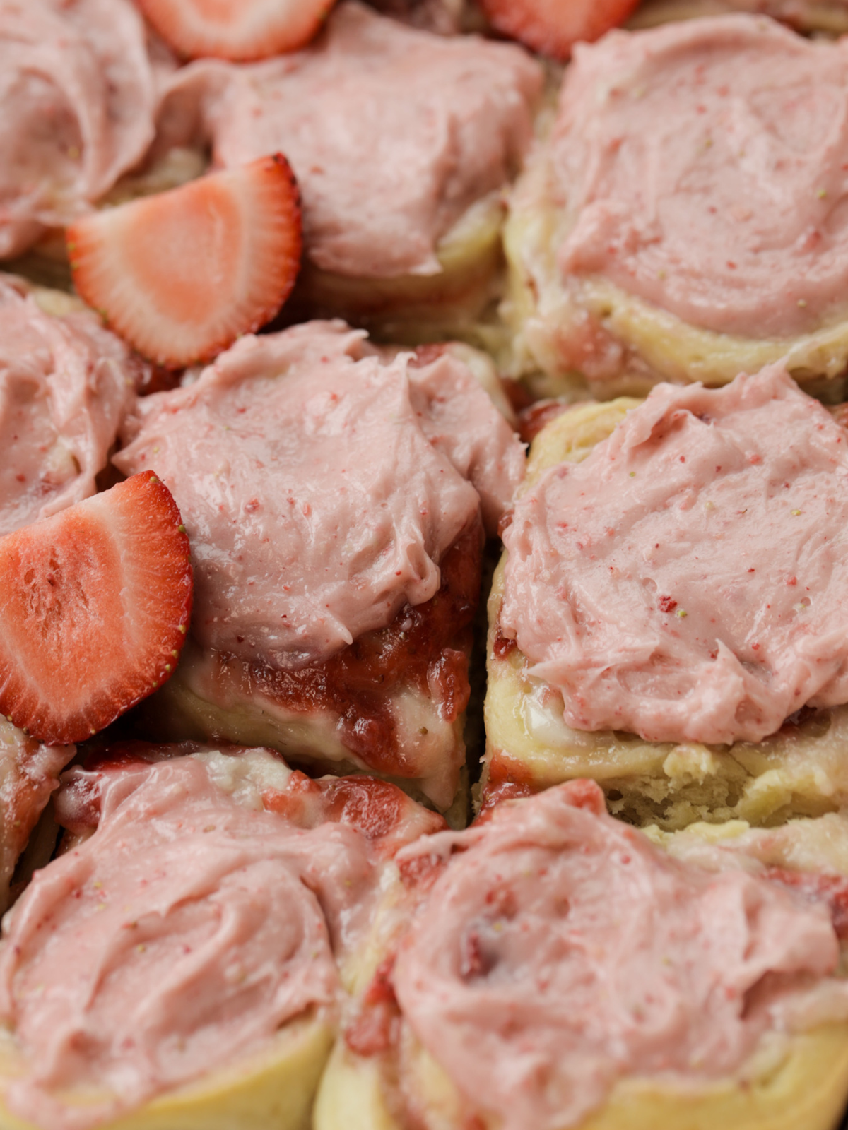 Naturally fermented sourdough strawberry cheesecake rolls sit in a baking pan. They're topped with a rich and creamy strawberry cream cheese frosting.