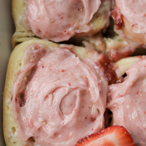 From-scratch sourdough brioche strawberry cheesecake sweet rolls sit in a 9x13 baking dish. They are frosted with a homemade strawberry cream cheese frosting.