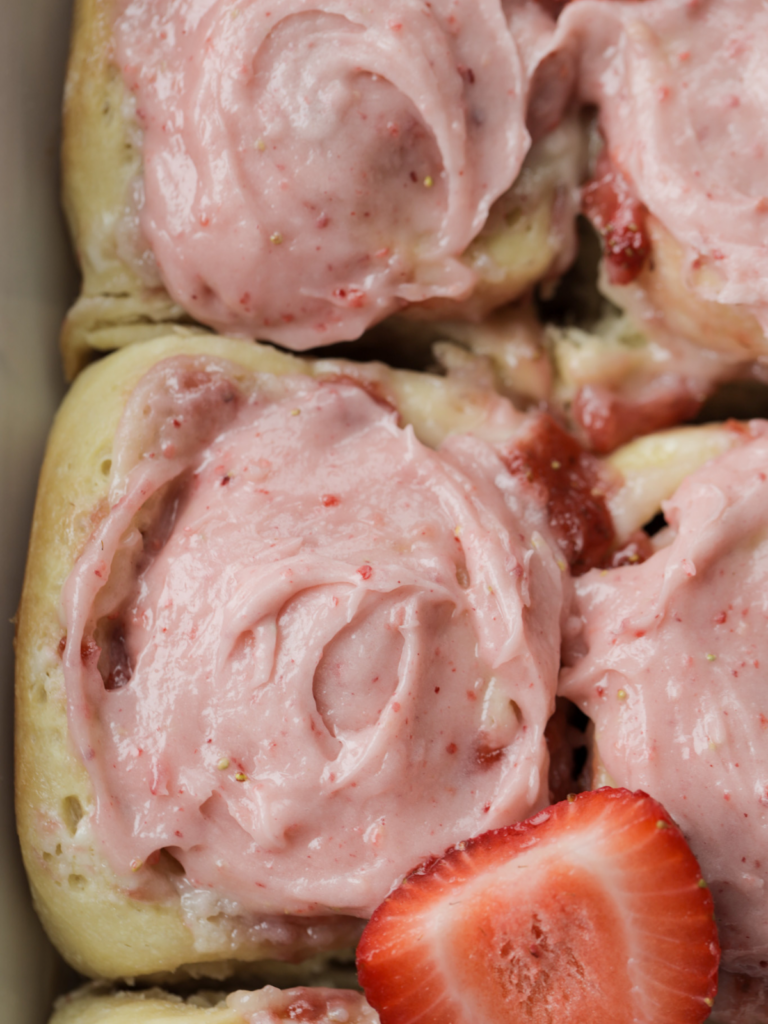 From-scratch sourdough brioche strawberry cheesecake sweet rolls sit in a 9x13 baking dish. They are frosted with a homemade strawberry cream cheese frosting.