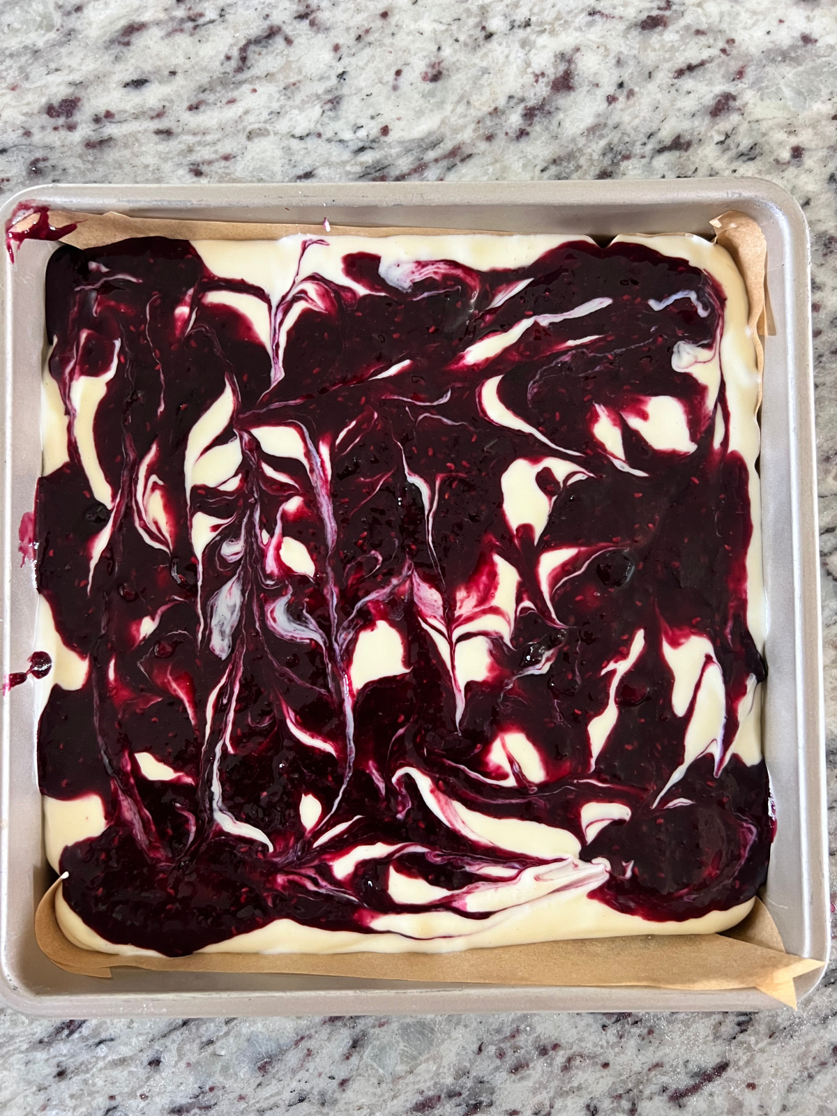 The berry sauce is shown swirled over the cheesecake filling.