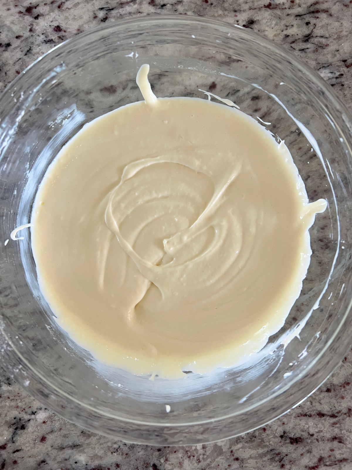 The cheesecake filling is shown in the glass mixing bowl smooth and ready to go into the pan to bake.