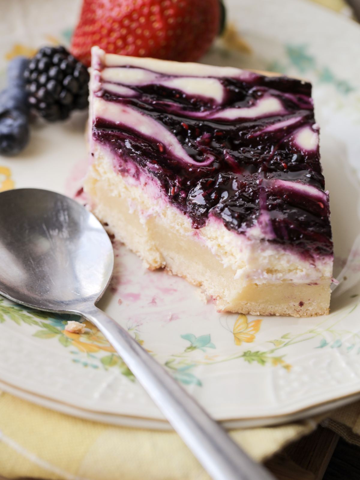 A partially eaten berry swirl cheesecake bar is shown on a floral plate. 