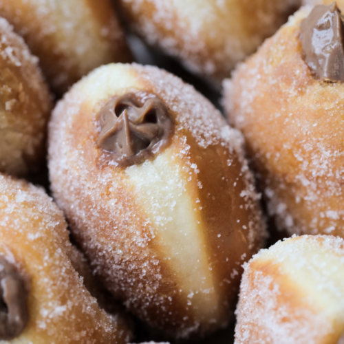 A closeup of a naturally fermented sourdough donut that is coated in granulated sugar and filled with a homemade chocolate custard. Several other donuts surround the one in focus.
