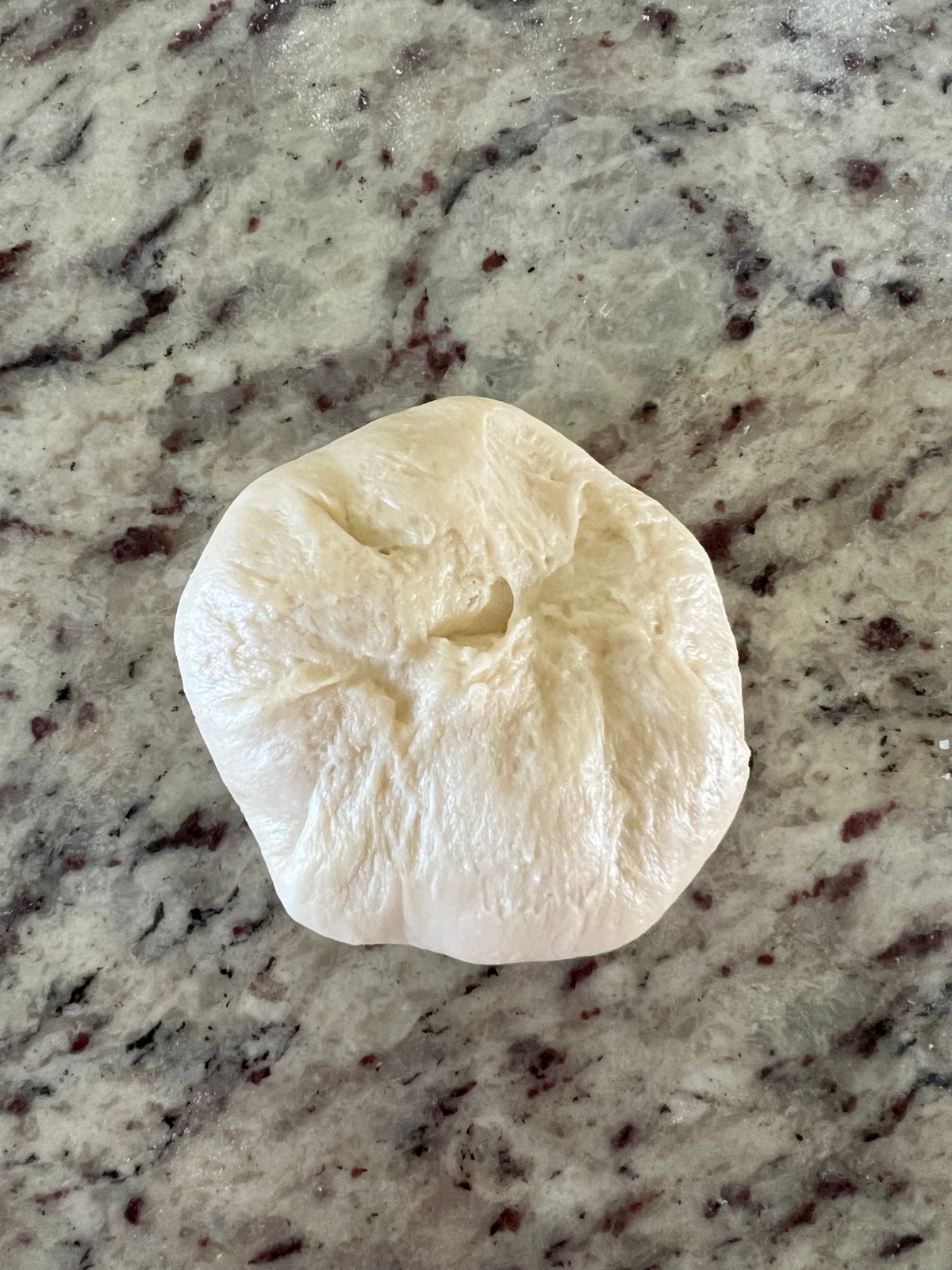 The stuffed dough ball has been pinched together at the seams so no filling will escape while baking.