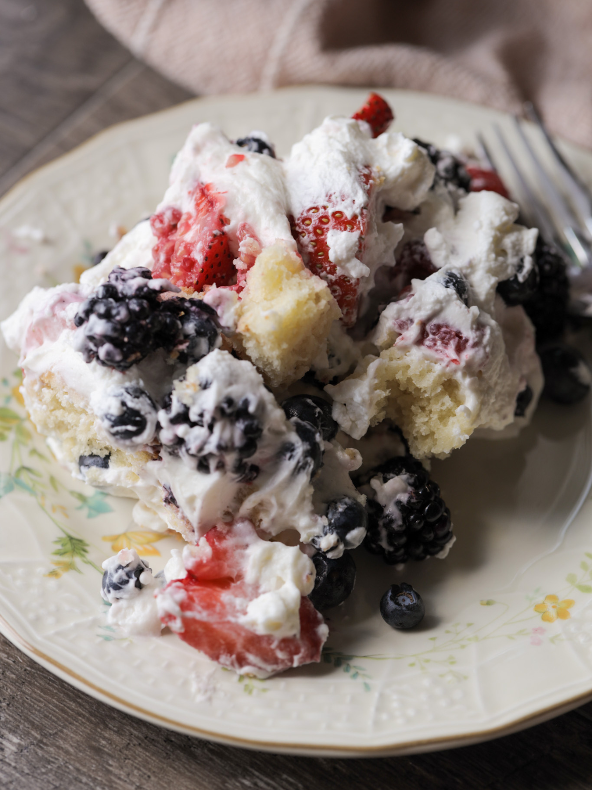 A plate of mixed berries and cream sourdough vanilla pound cake trifle is shown on a floral plate.
