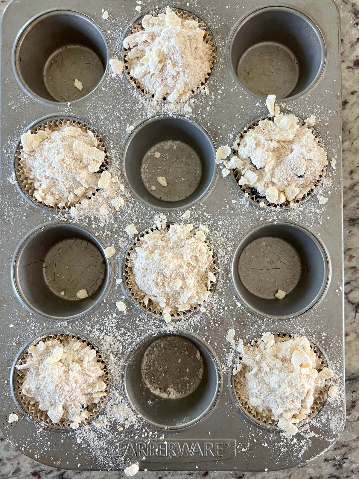The sourdough blueberry muffin batter is shown in the muffin pan. Every other cup is filled with batter and then topped with the crumble topping.