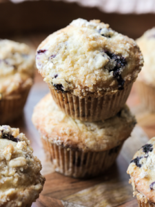 Two sourdough discard blueberry muffins are shown stacked with several other muffins in the background.