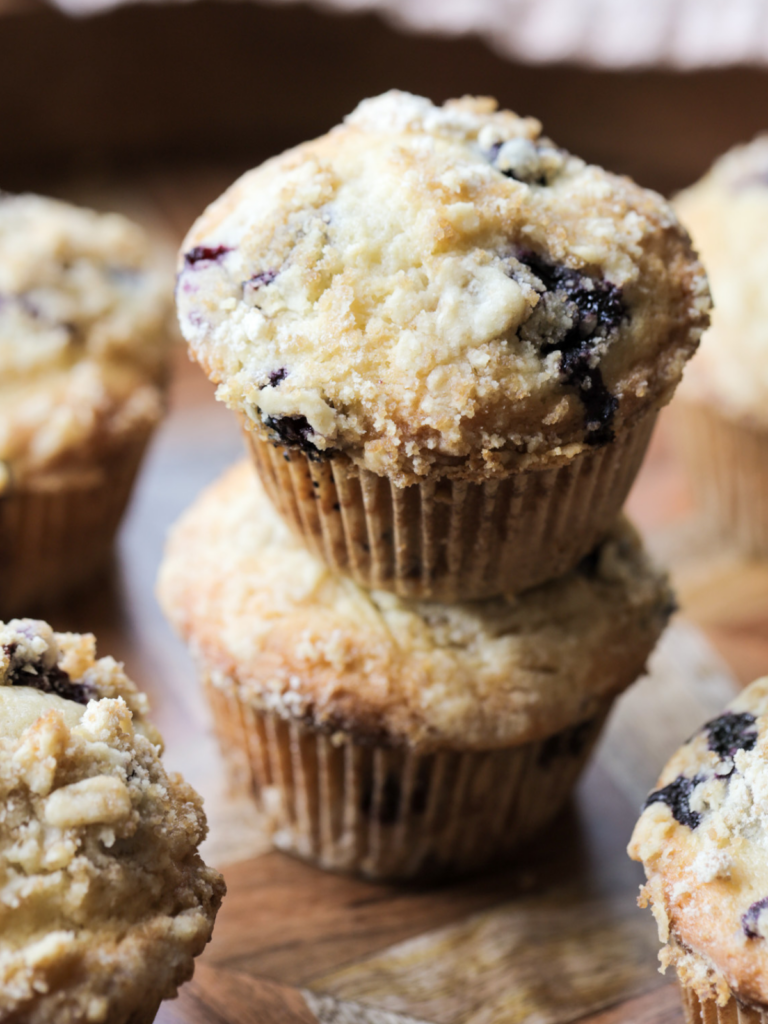Two sourdough discard blueberry muffins are shown stacked with several other muffins in the background.