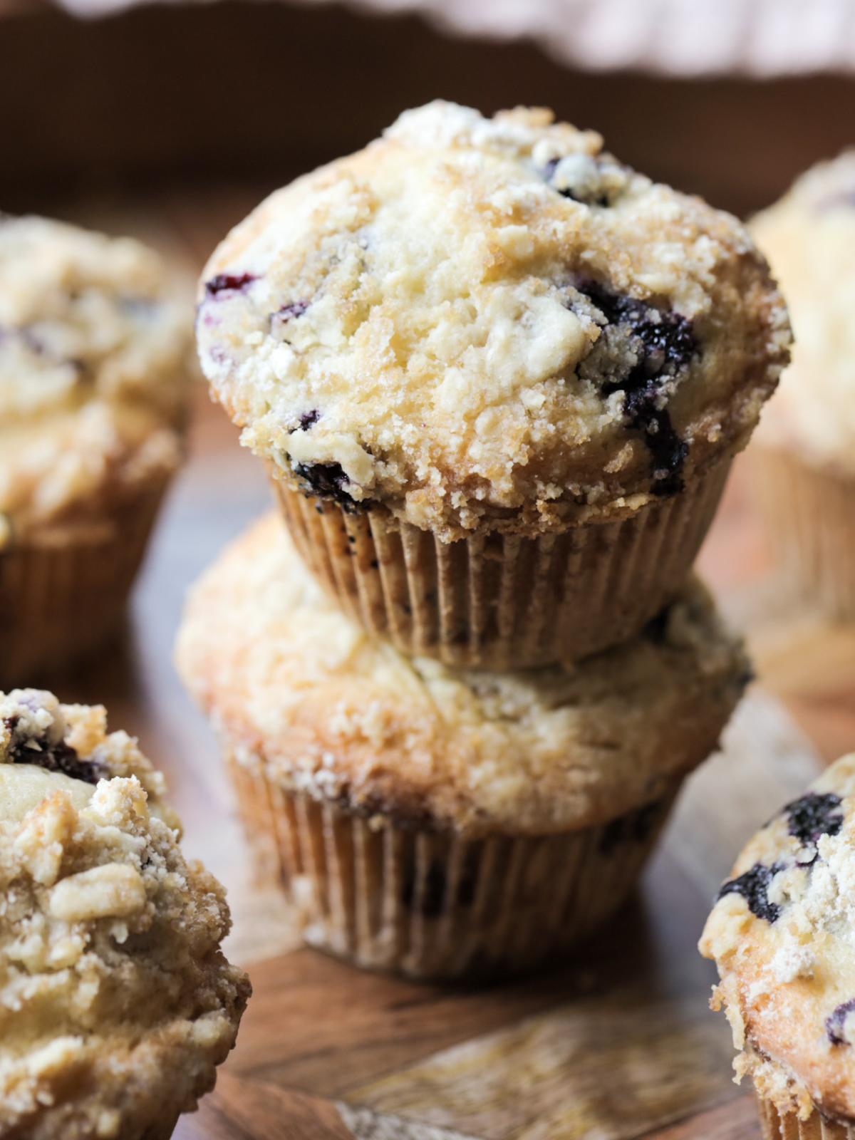 Two sourdough discard blueberry muffins are shown stacked with several other muffins in the background.