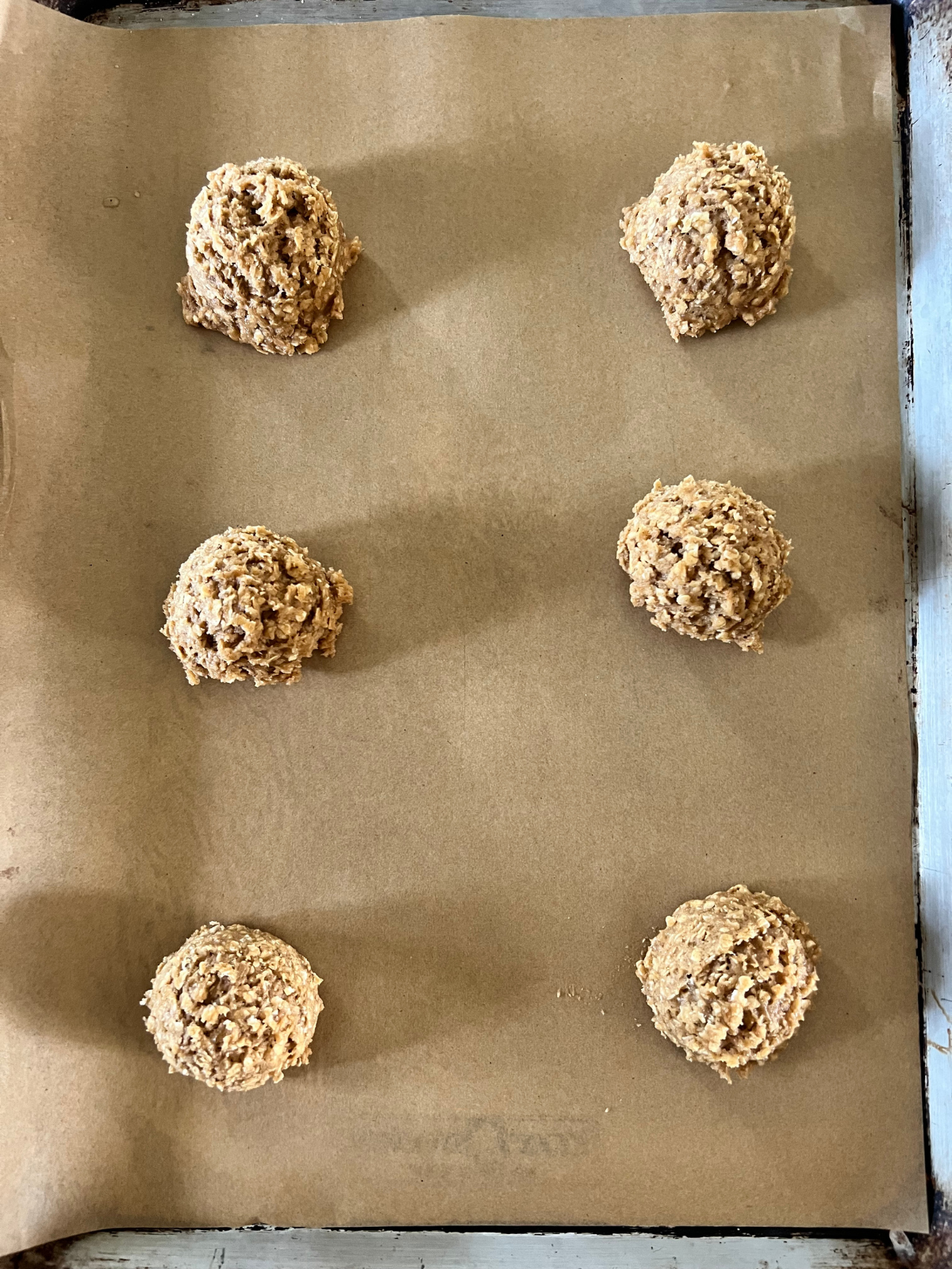 The sourdough oatmeal cookies are shown scooped into 3 tablespoon portions on a parchment-lined baking sheet---6 cookie dough balls.