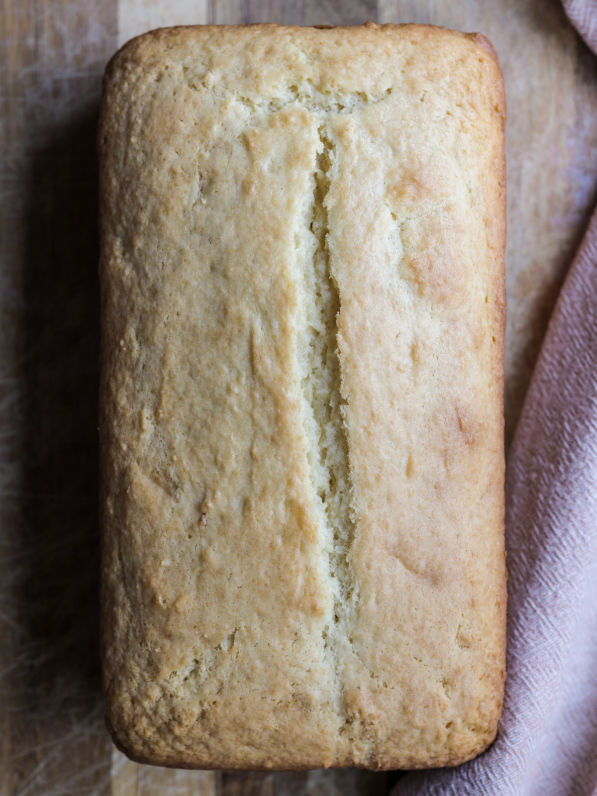 A full loaf of sourdough discard vanilla pound cake sits on a wooden cutting board.