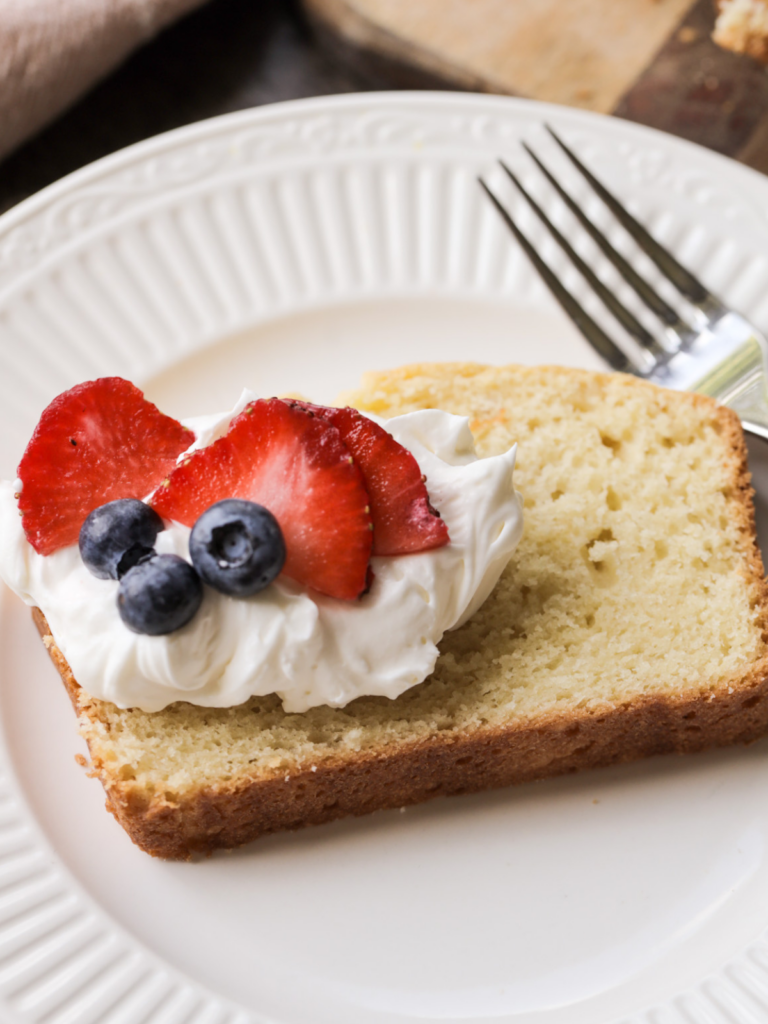 From scratch sourdough discard vanilla pound cake is shown with whipped cream and berries on top of the slice.
