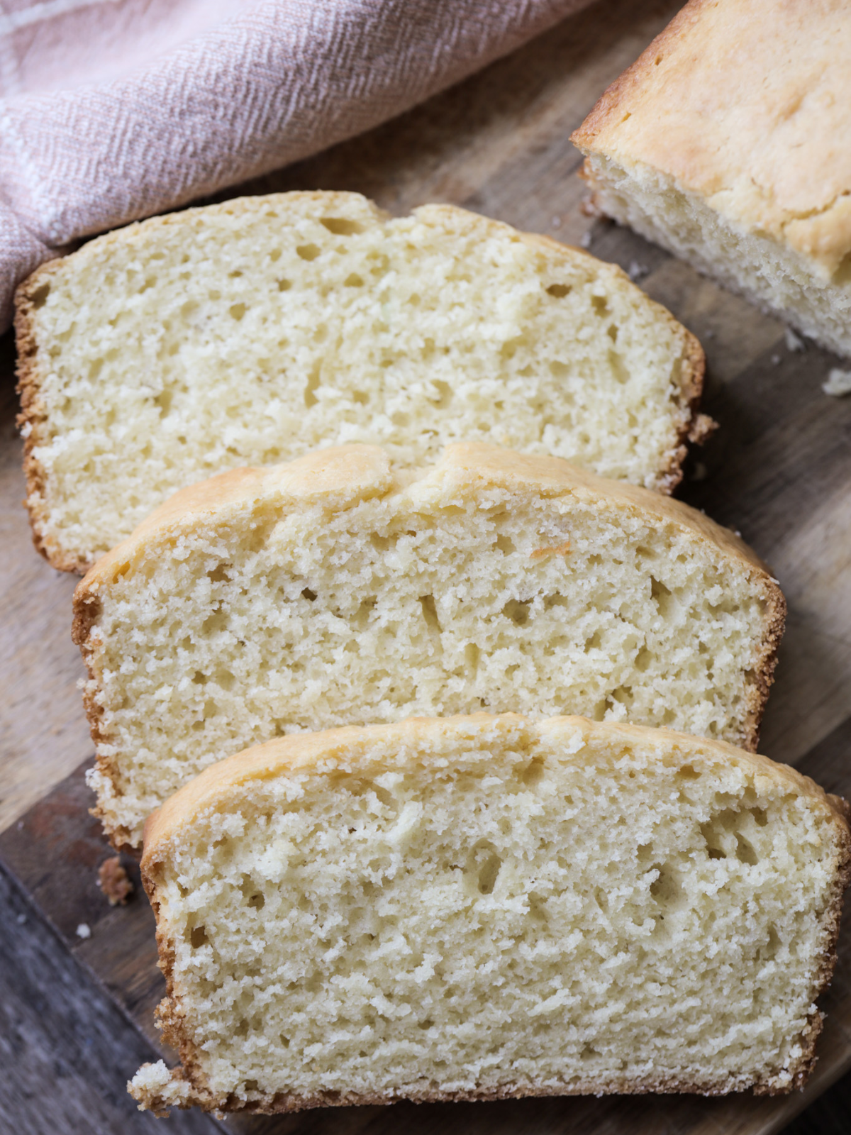 Three slices of sourdough vanilla pound cake rests on a wooden cutting board.