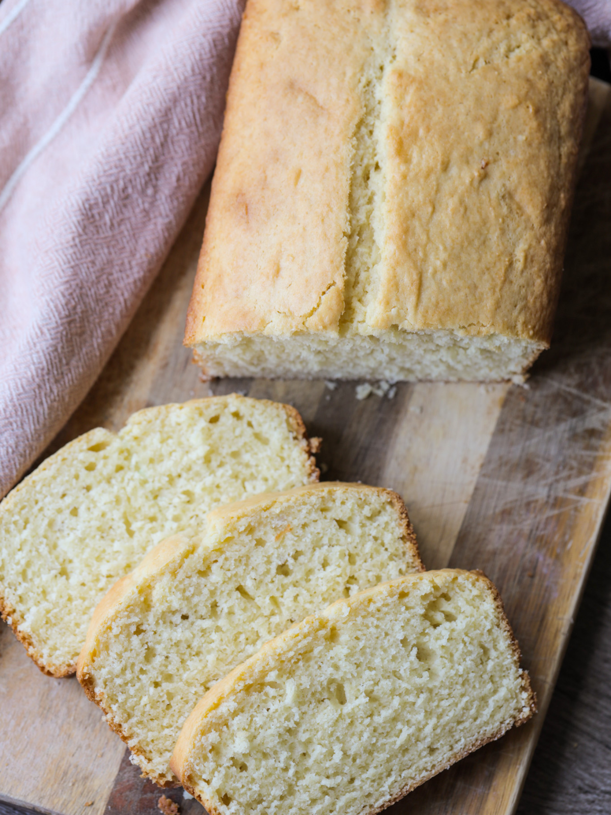 Three slices of sourdough discard vanilla pound cake is shown next to the rest of the loaf on a wooden cutting board.