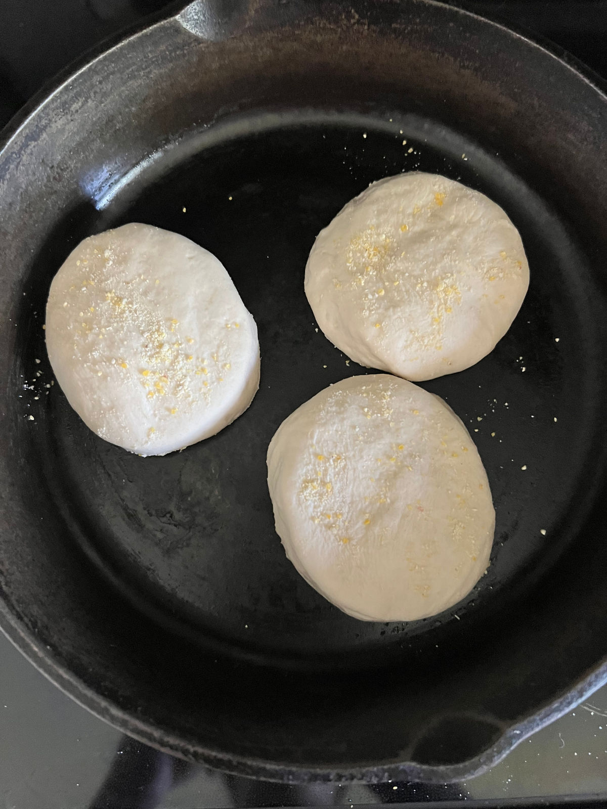 The English muffins are shown on a cast iron pan cooking on the first side.