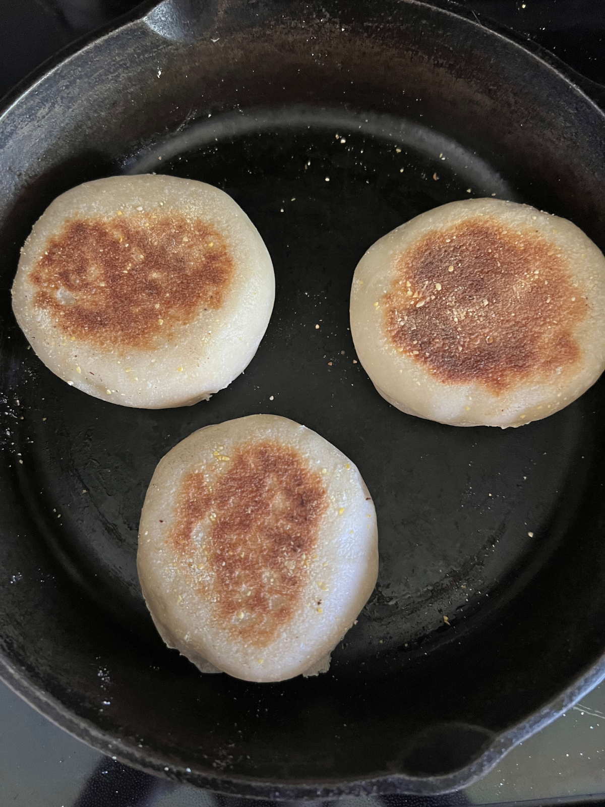 The English muffins are shown on the cast iron skillet cooking on their second side. You can see the golden brown on the outside--the classic English muffin look!
