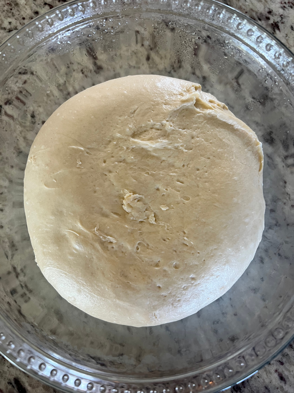 The bulk fermented sourdough sticky bun dough is shown in a glass mixing bowl.