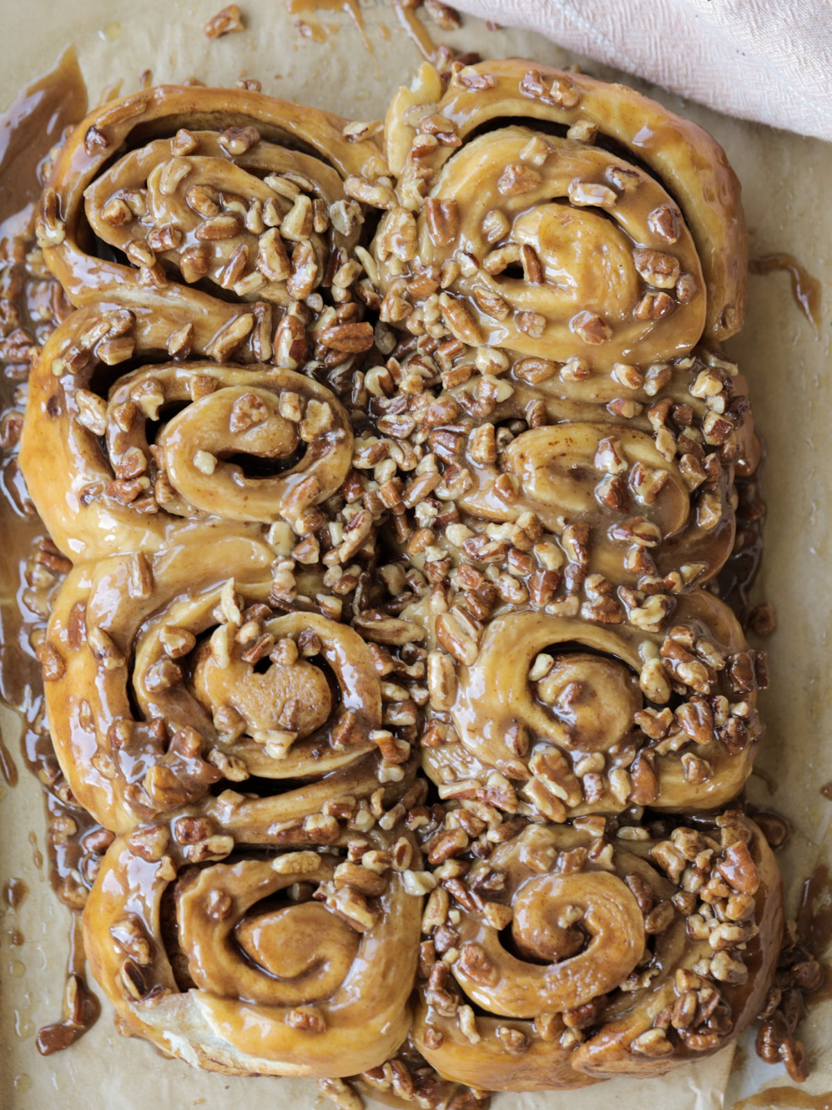 The freshly baked sourdough sticky buns are shown on parchment paper with the gooey caramel and pecans.