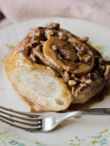 A closeup of a sourdough pecan sticky bun is shown. It has a soft, fluffy interior and is covered in a homemade caramel and chopped pecans.