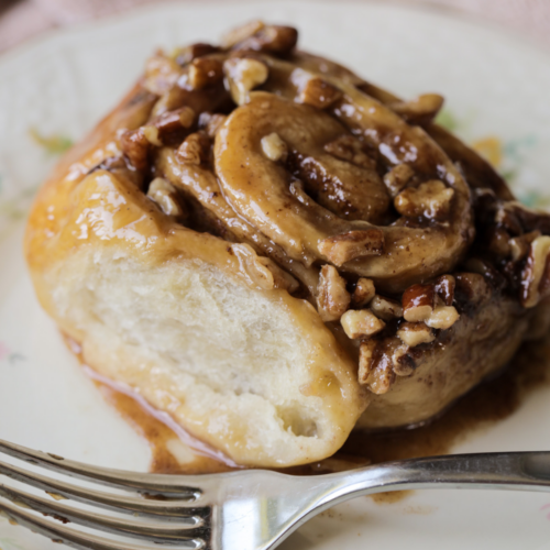 A closeup of a sourdough pecan sticky bun is shown. It has a soft, fluffy interior and is covered in a homemade caramel and chopped pecans.