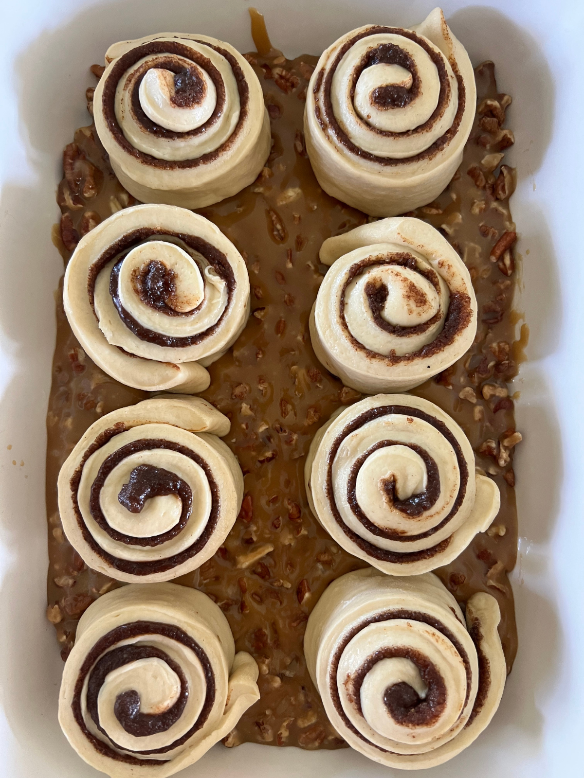 The shaped sourdough sticky buns are shown placed on top of the caramel pecan sauce in the pan.
