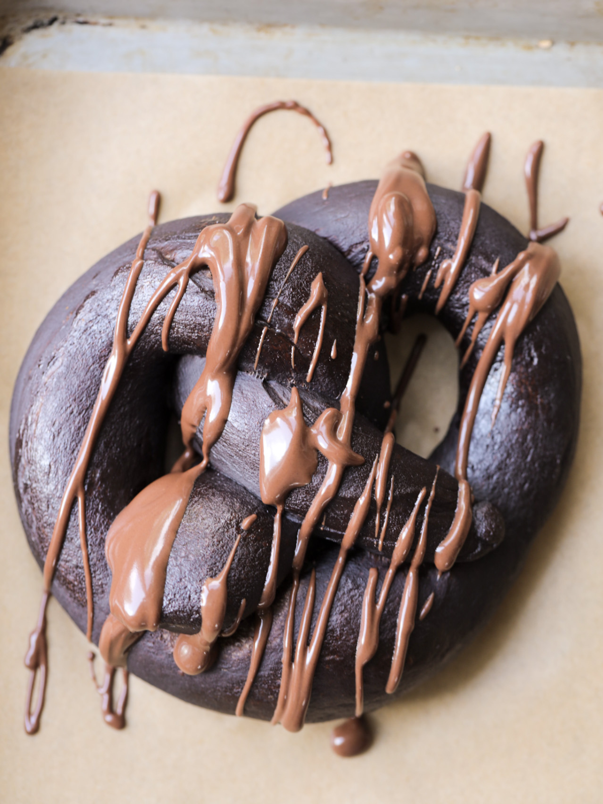 A closeup of a sourdough chocolate soft pretzel is shown with chocolate drizzled over it.