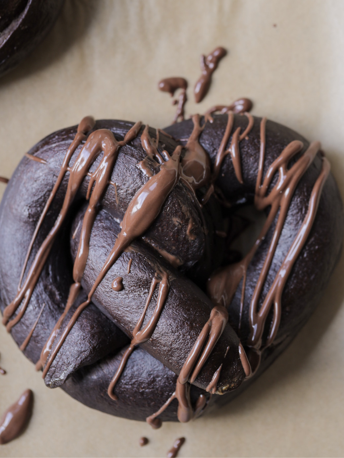 A 100% sourdough chocolate soft pretzel with chocolate drizzled over it is shown closeup.