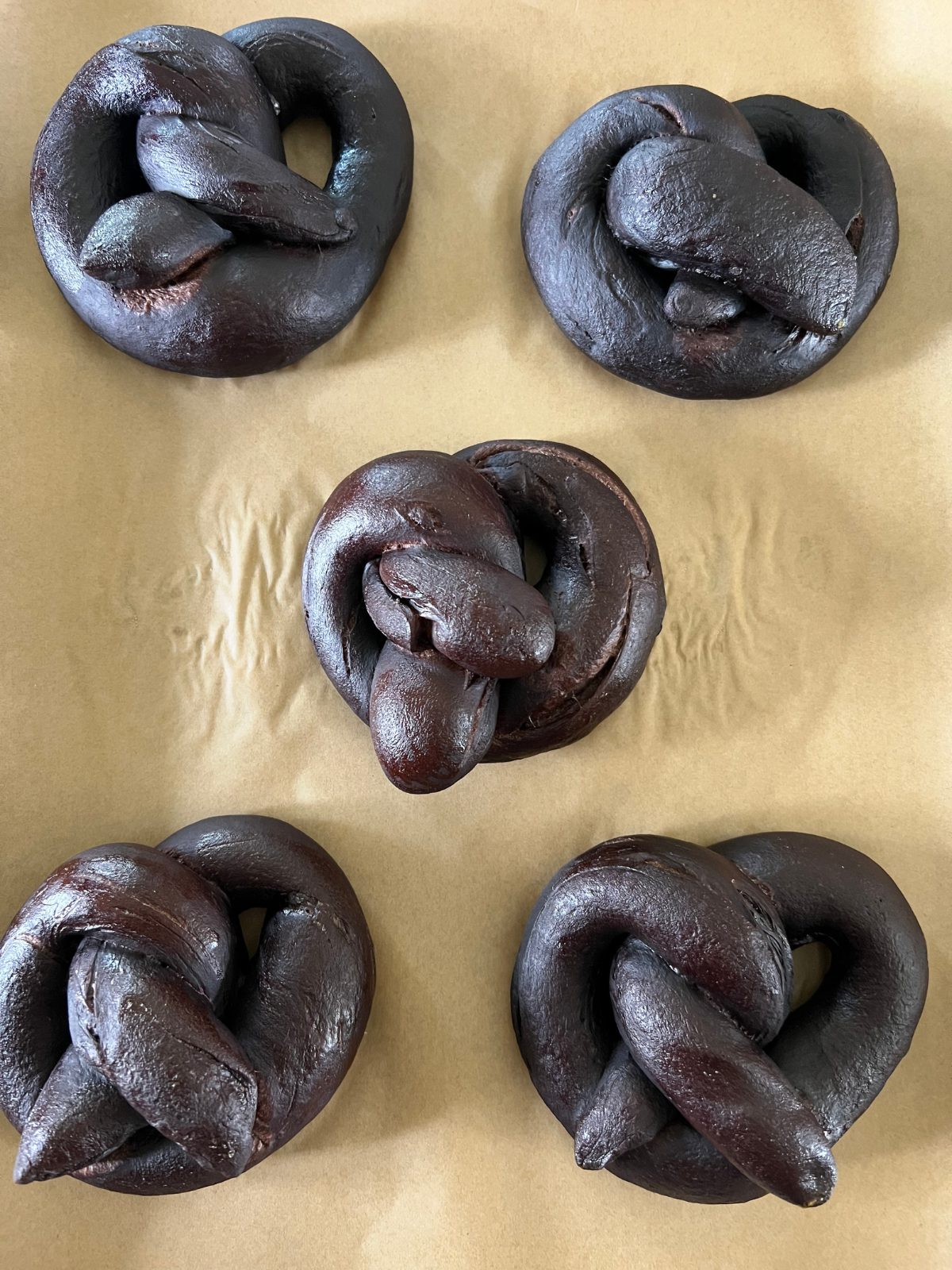 Five sourdough chocolate pretzels are shown after baking on a baking sheet.
