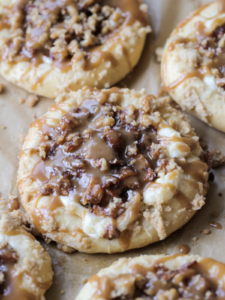 A closeup of a sourdough cream cheese caramel apple kolache is shown on a parchment paper lined baking sheet.