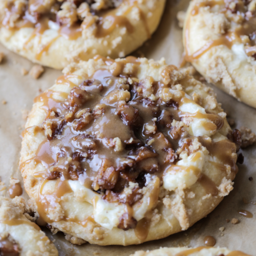 A closeup of a sourdough cream cheese caramel apple kolache is shown on a parchment paper lined baking sheet.