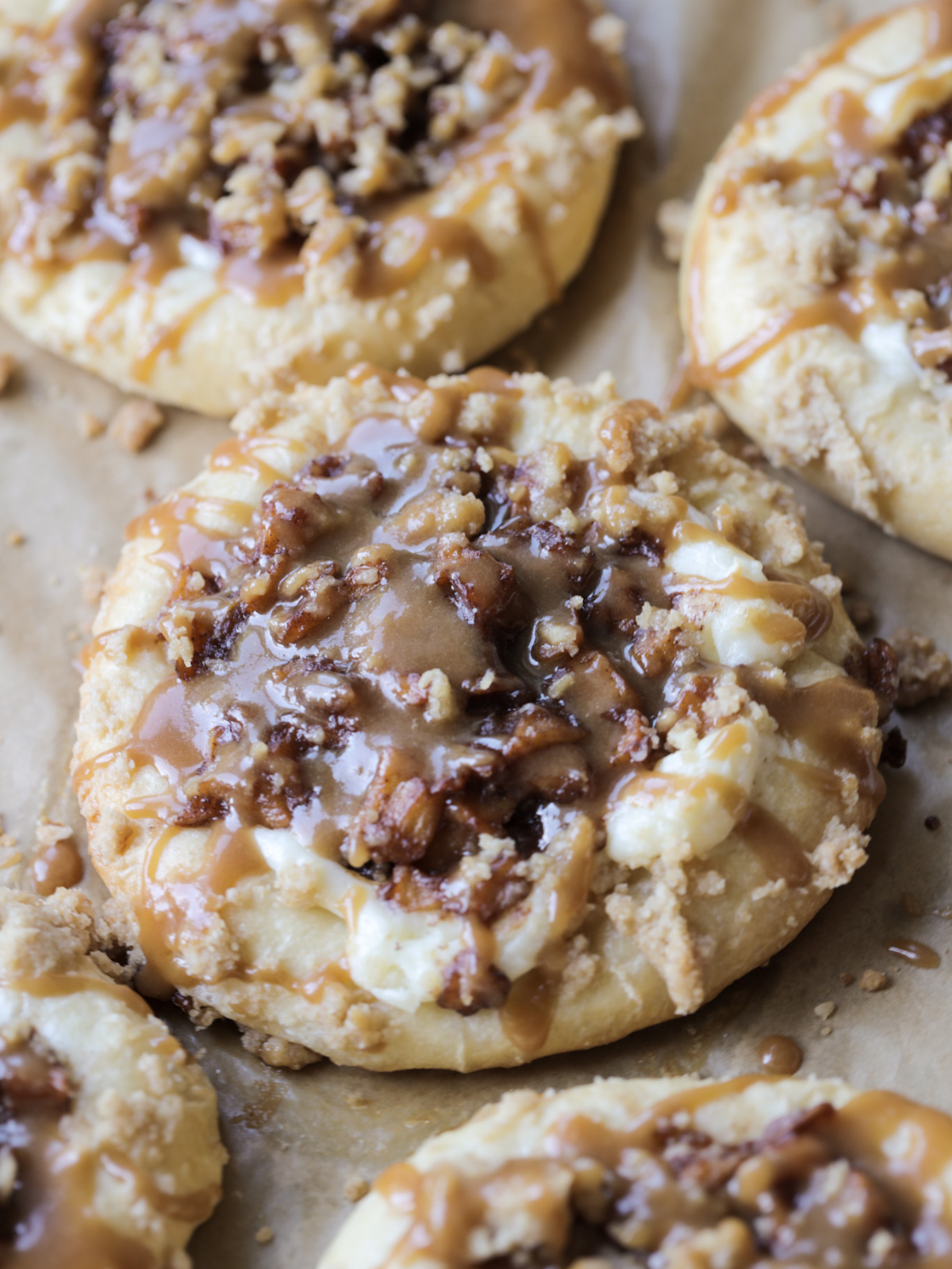 A closeup of a sourdough cream cheese caramel apple kolache is shown on a parchment paper lined baking sheet.