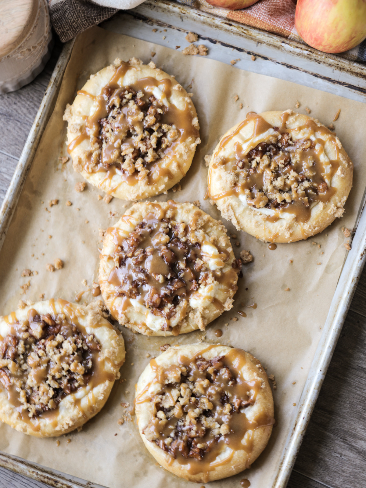 Five sourdough brioche caramel apple crumble kolaches are shown on a parchment lined baking sheet.