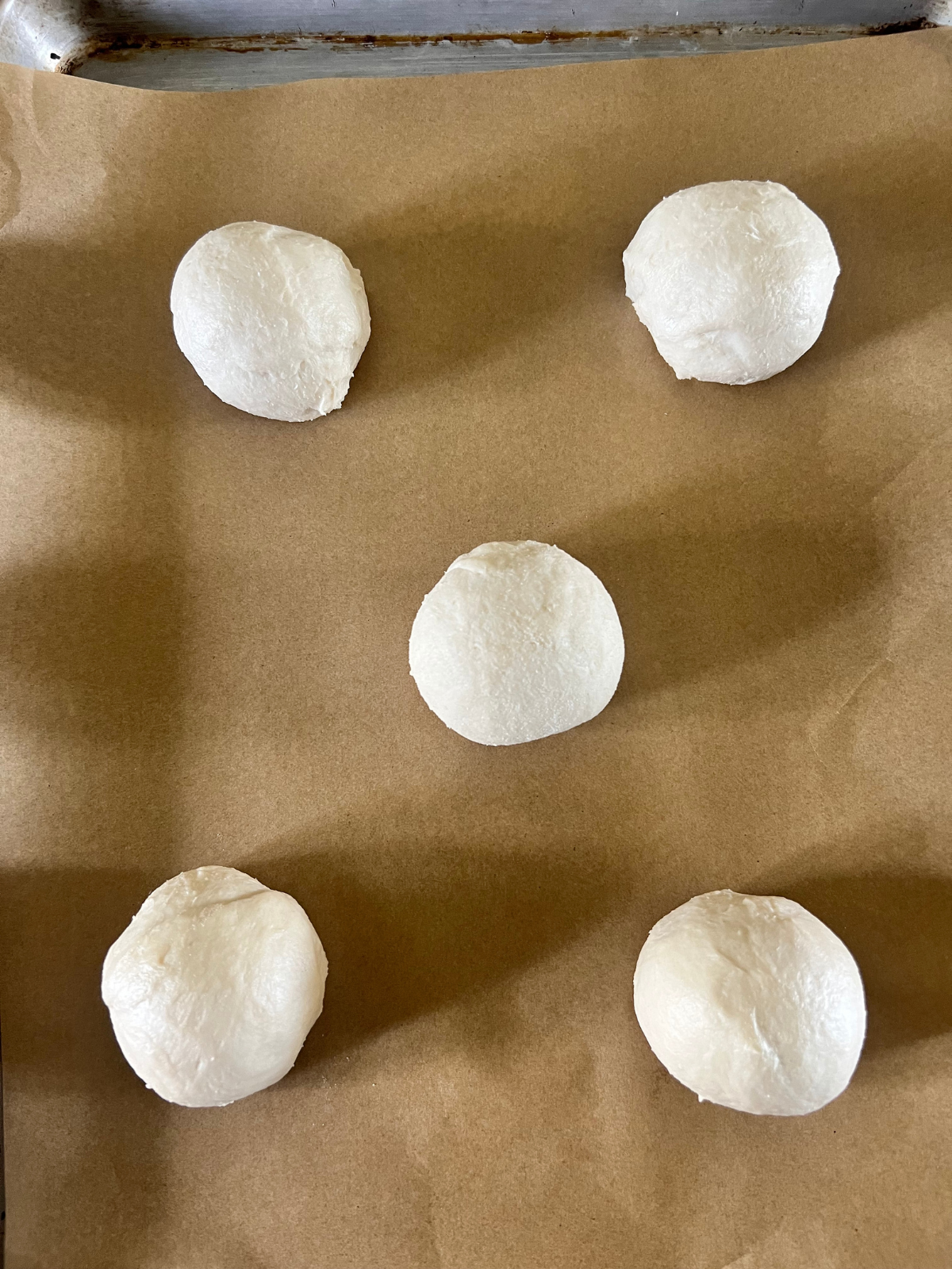 The sourdough brioche caramel apple kolache dough balls are shown placed on a parchment paper lined baking sheet preparing for their second rise.