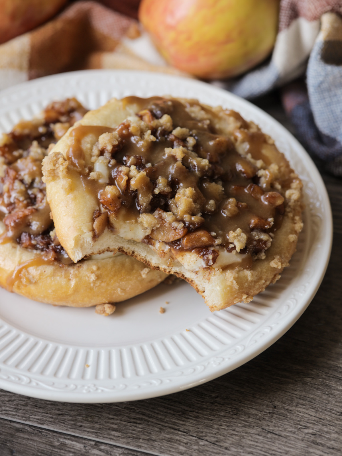 Two sourdough caramel apple cream cheeese kolaches are shown on a plate. The top kolache is shown with bites taken out of it.
