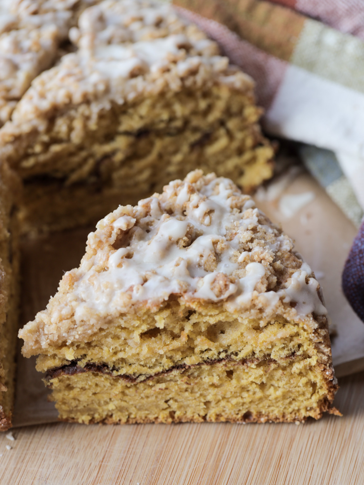 A closeup of the sourdough discard pumpkin coffee cake with vanilla icing is shown sitting on a wooden cutting board.