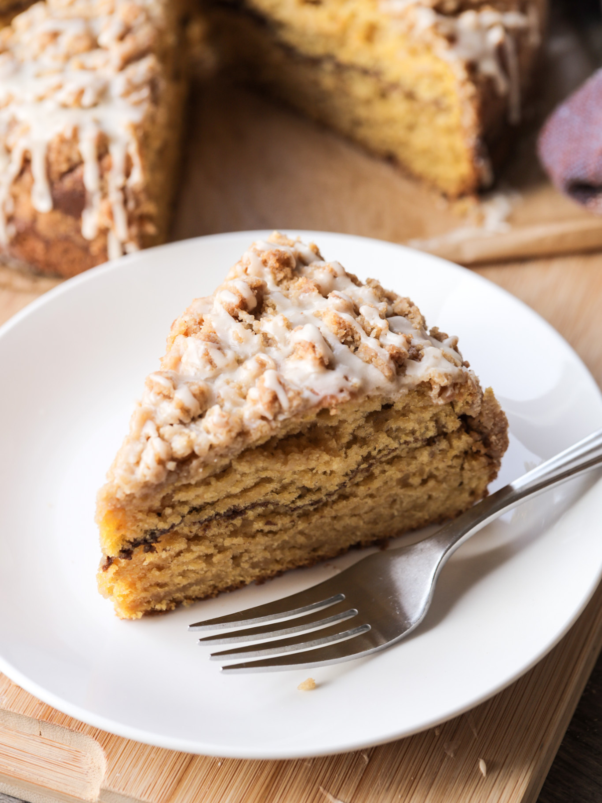 A slice of sourdough pumpkin coffee cake sits on a plate with the cake in the background. 