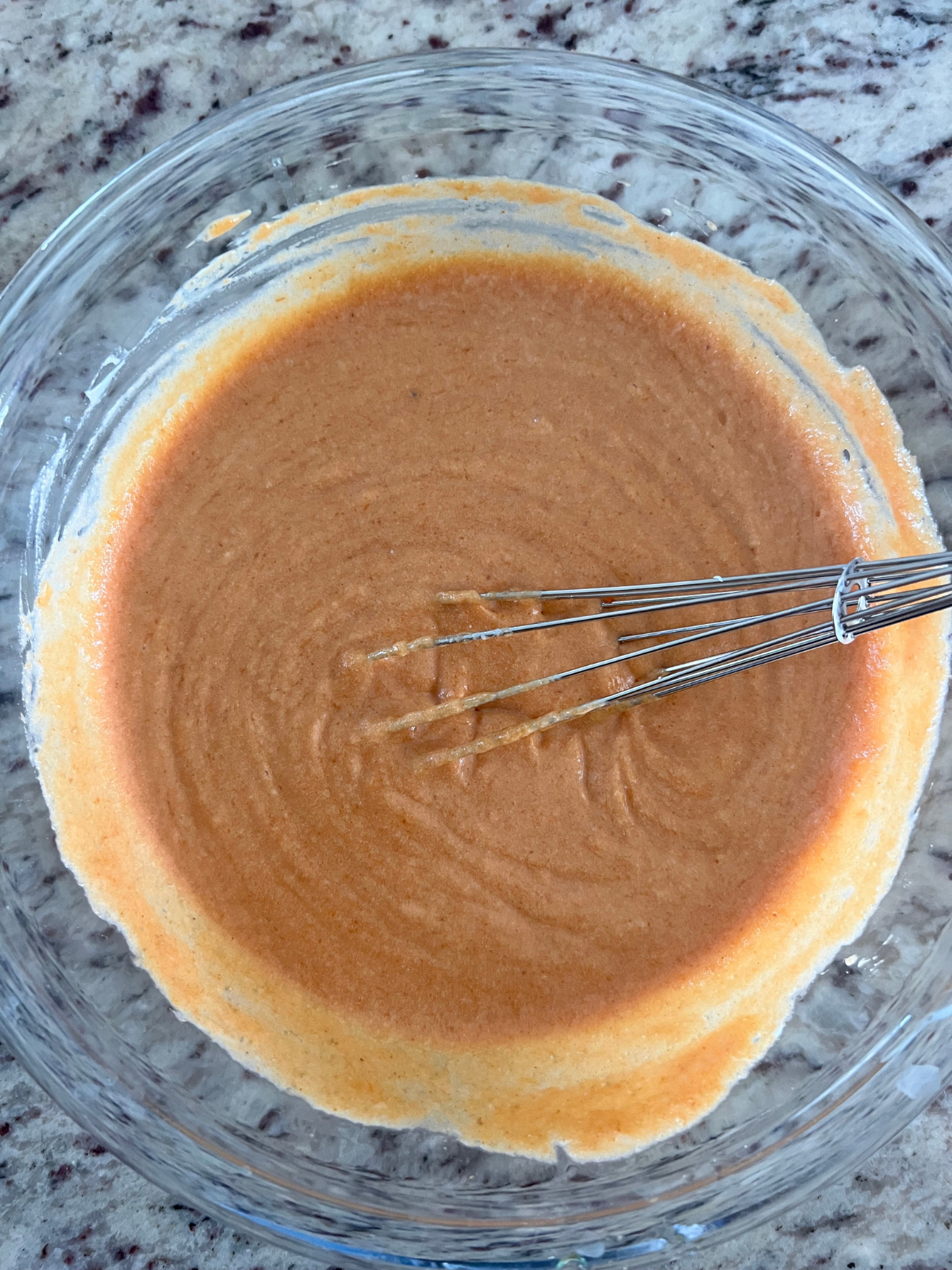 The wet ingredients for the sourdough discard pumpkin coffee cake sit in a glass mixing bowl.