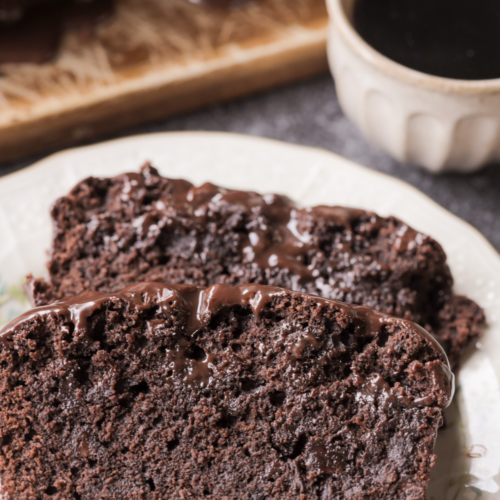 Sourdough discard chocolate fudgy brownie bread is shown with two slices cut out and sitting on a plate. A cup of coffee rests in the background.