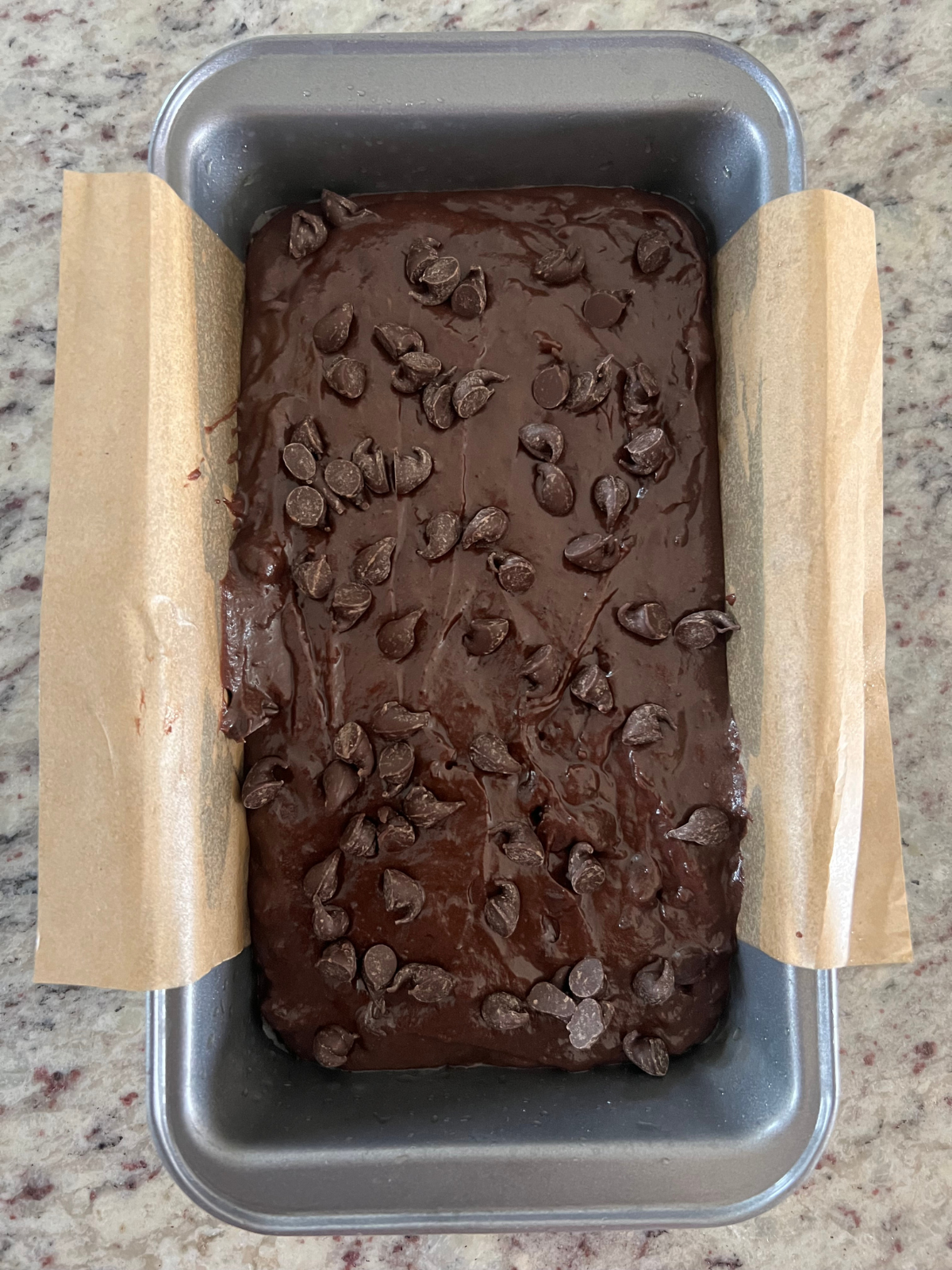 The sourdough fudgy brownie bread batter sits in a 9x5 metal loaf pan lined with parchment paper.